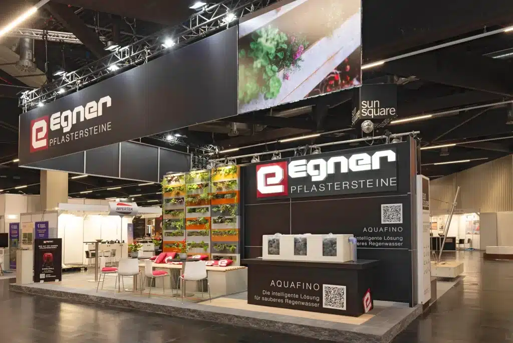 Gesamtansicht des Egner-Stands auf der GaLaBau Nürnberg mit Deckenblende, Videowand und Sitzbereich vor der Begrünungswand.