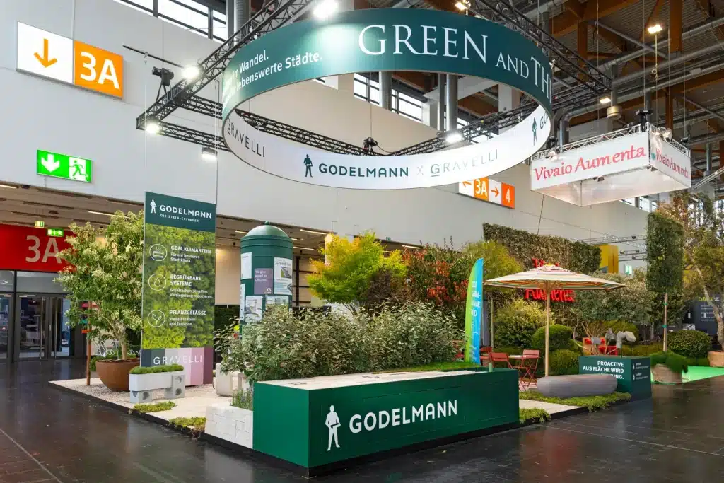 Messestand von Godelmann auf der GaLaBau in Nürnberg mit rundem Deckenring Green and the City, begrünter Standfläche und grüner Thekenwand.