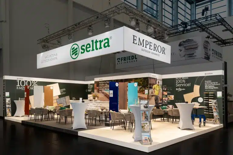 Messestand der seltra Natursteinhandel GmbH auf der GaLaBau in Nürnberg mit umlaufendem Deckenblender, Loungemöbeln und Natursteinmustern.
